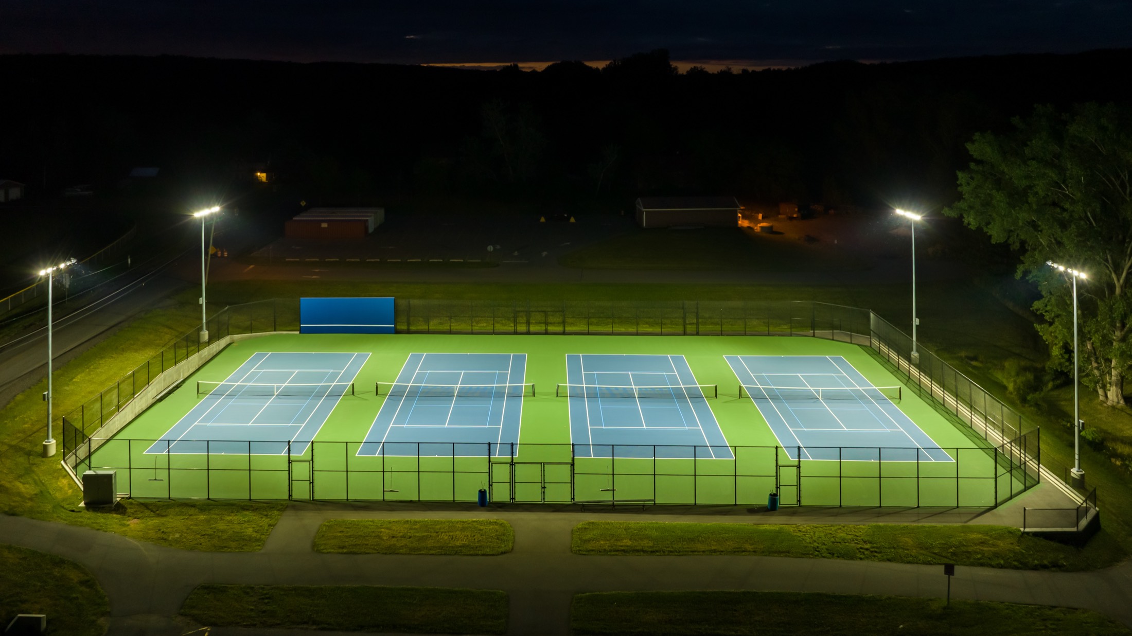 Aerial view of lit tennis and pickleball courts at night
